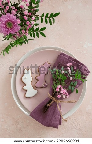 Easter table setting with flowers and bunny icing cookies. Spring holiday concept. Flat lay. Pink background, top view, copy space
