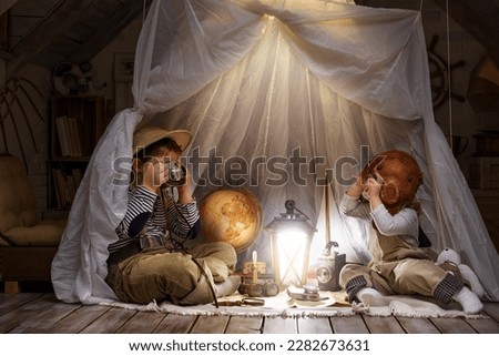 Children play in the attic of their house. Imagine themselves as tourists, explorers. Look through a telescope, study a world map, play in a makeshift tourist tent. Dreaming of travel and adventure. Royalty-Free Stock Photo #2282673631