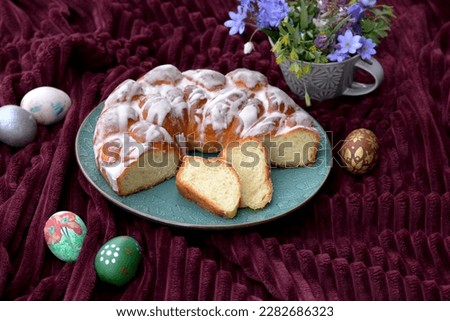 Bread texture of sliced Easter bread with sugar glaze in a shape of wreath with Easter eggs. Sweet bread sliced with Easter eggs and flowers. Home baked braided bread with two slices of Easter cake. Royalty-Free Stock Photo #2282686323
