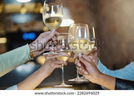 Close-up detail of diverse hands, including a dark-skinned person, toasting with glasses of white wine in a pub or restaurant with nighttime lighting. Royalty-Free Stock Photo #2282696029