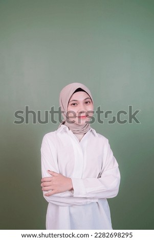 a beautiful Asian woman in a hijab is posing with a smiling expression in front of a gray background