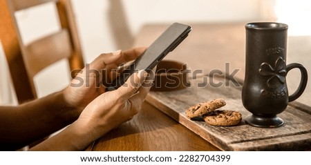 hands holding phone, oatmeal cookies and cup for irish coffee in the background.
