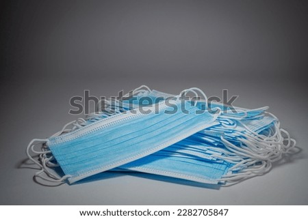 Blue surgical masks with rubber ears straps  stacked in layers on middle gray background.