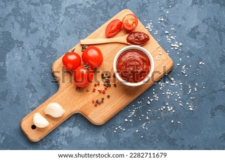 Composition with bowl of tasty tomato paste, spoon, peppercorns and salt on blue grunge background Royalty-Free Stock Photo #2282711679
