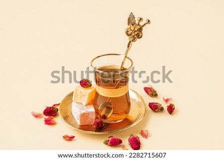Glass cup of tea with roses and Turkish delight on beige background