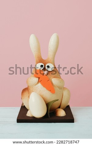 a white chocolate bunny as a spanish mona de pascua, a traditional confection given by godparents to godchild on easter, on a table against a pink background