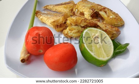 fried fish called kurisi fish served on a white plate with delicious tomatoes and oranges