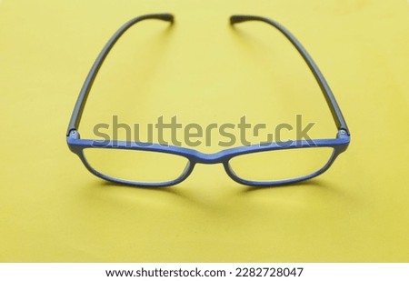 close up and flat lay a modern glasses,eyewear,spectacles,spectacles,glasses 
blue frames fashion for men and women over the bright yellow background