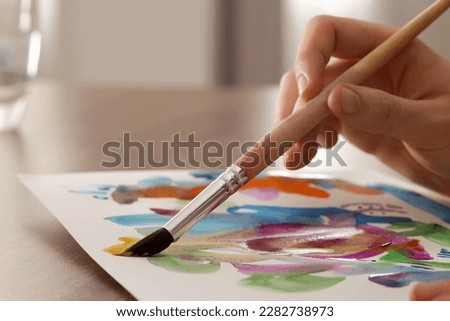 Woman painting with watercolor at wooden table indoors, closeup
