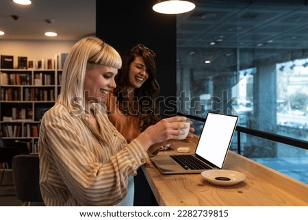 Cheerful student girl showing learning online presentation on laptop computer to classmate, holding digital gadget, looking at screen, smiling, using device in college school library books store