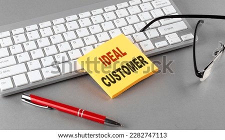 IDEAL CUSTOMER text on sticky with keyboard, pen glasses on grey background