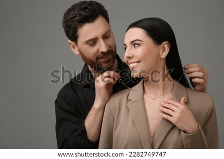 Man putting elegant necklace on beautiful woman against dark grey background Royalty-Free Stock Photo #2282749747