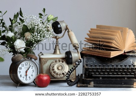 Still life with retro objects on a desk. Vintage typewriter, red apple and white flowers close up photo. 
