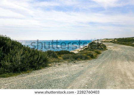 Winding Gravel Road Along the Coast of Agios Georgios Alamanou with Green Bushes and Bright Landscape on the Endless Azure Mediterranean Sea with Blue Sky (Monagroulli, Limassol District, Cyprus) Royalty-Free Stock Photo #2282760403