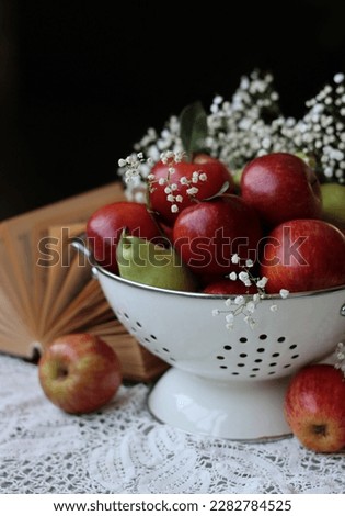 Organic pears and apples in a white metallic colander. Close up photo of seasonal fruit on a table. Colorful still life with apples and Gypsophila flowers. Natural vitamins and antioxidants concept. 