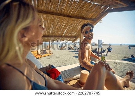 Couple enjoying vacation. Young man and woman sitting on sunbeds at beach. Holiday, lesiure, lifestyle concept.