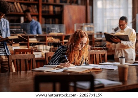 A young adult female student is sitting at the table in the library, studying for her upcoming exams.