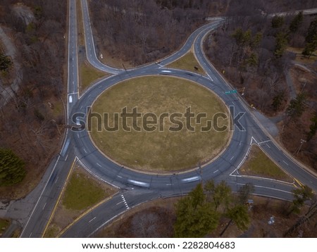 An aerial view of a large roundabout in the mountains in upstate New York during the end of the fall season. There are dry brown trees in the surrounding area. Taken with a drone camera.