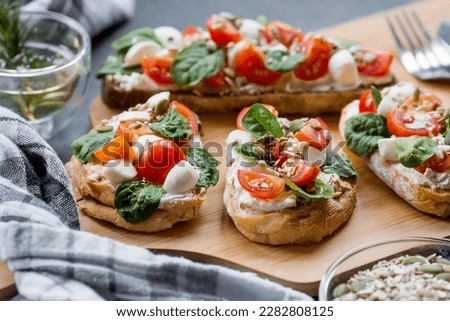 Bruschetta (sandwiches) with cherry tomatoes, mozzarella cheese and herbs on a cutting board on a dark background. Traditional Italian snack. Royalty-Free Stock Photo #2282808125