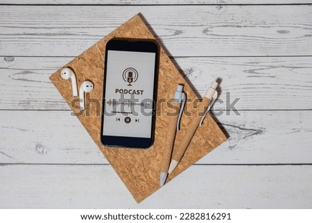 Paper notebook pens with wireless headphones and mobile phone Podcast listening website page app application. Audio healing, sound therapy wellness rituals, positive mental health habits