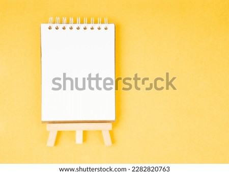 Spiral notebook with blank empty white sheets on a bright yellow background, top view, flat lay with copy space.