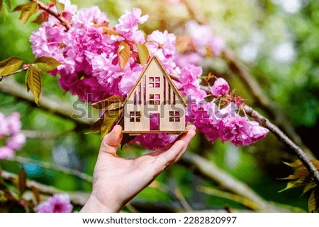 The girl holds the house symbol against the background of blossoming Sakura
