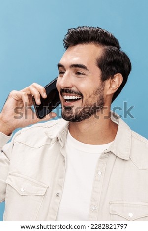 Portrait of a brunette man close-up talking on the phone smile with teeth joy and laughter victorious fist up, on a blue background in a white T-shirt and jeans, copy space