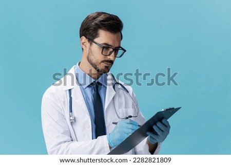 Male doctor in a white coat and glasses with a medical record on a blue isolated background, copy space, space for text