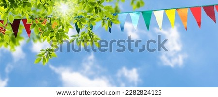 colorful pennant string decoration in green tree foliage on blue sky, summer party background template banner with copy space Royalty-Free Stock Photo #2282824125