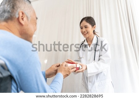 Selective focus, Beautiful female doctor receives a gift box from senior man in a wheelchair, they smile happily at each other, copy space