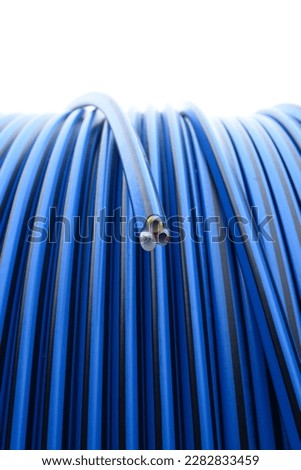 Close up on outdoor blue and black colored optical fiber tube coil with 3 tubes inside, blue, yellow and red striped Royalty-Free Stock Photo #2282833459