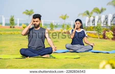 Young couple doing yoga or pranayama with eyes closed during morning at park - concept of healthy lifestyles, mindfulness and morning rituals Royalty-Free Stock Photo #2282836543
