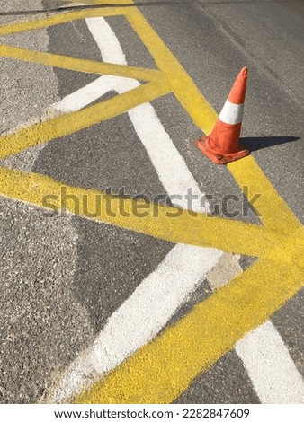 High angle view over white and yellow road lines for construction works. Orange plot in the middle of the stripes, grey asphalt in background. Caution, road works and interdiction to park here.