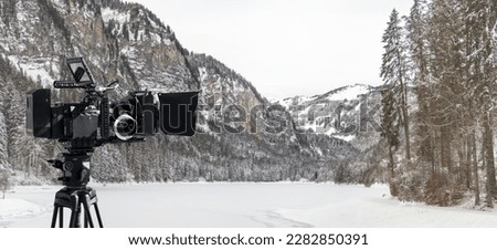 Digital film camera filming winter in the mountains near a frost lake. Wide panoramic view for tv show production banner or documentaries background