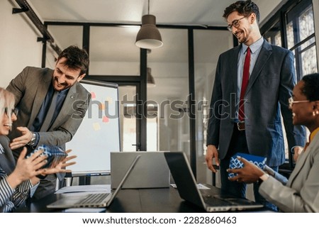 Two handsome businessmen walk into an office, holding gifts and about to surprise their female coworkers. 