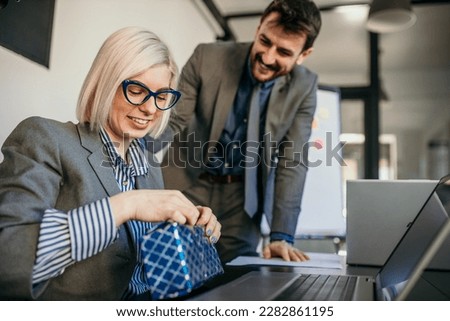 Young businessman giving his colleague present in the office. A young man surprised a beautiful businesswoman in the office.