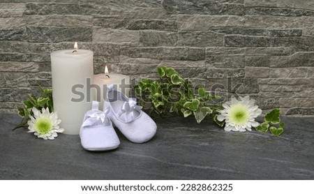 White booties with candles and flowers in front of a gray stone wall with space for text. Royalty-Free Stock Photo #2282862325