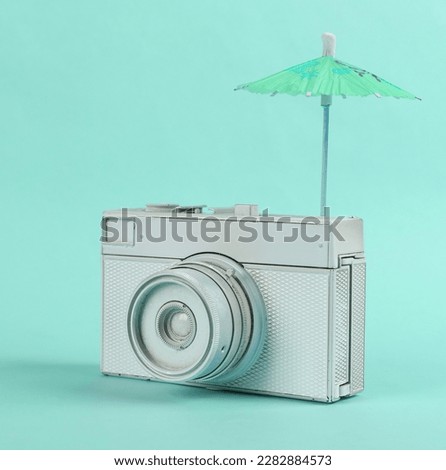 Retro camera with cocktail umbrella on a mint green background. Minimal travel still life, creative layout