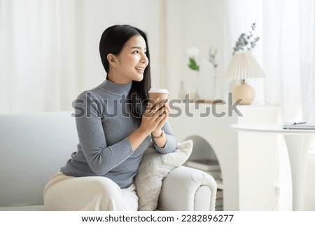 Young Asian woman drinking coffee while sitting at her couch.
