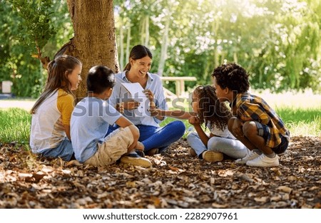 Books, reading or teacher with children in a park storytelling for learning development or growth. Smile, tree or happy educator with stories for education at a kids kindergarten school in nature Royalty-Free Stock Photo #2282907961