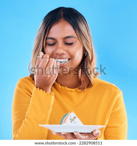 Birthday, blue background and a woman eating cake in studio while having fun at a party for celebration. Dessert, food and fork with an attractive young female enjoying a rainbow pastry snack Royalty-Free Stock Photo #2282908511