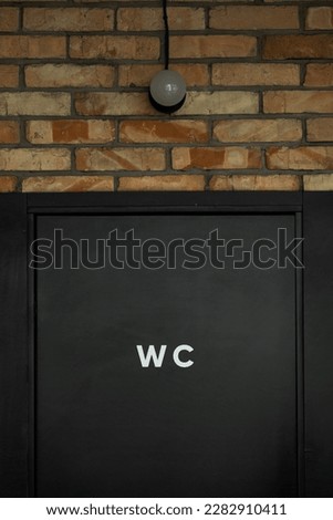 Black restroom door with a WC sign on it. Modern public toilet entrance. 
Loft style interior design