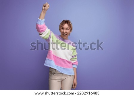 successful charming blond young woman raised her hand into a fist on a purple background