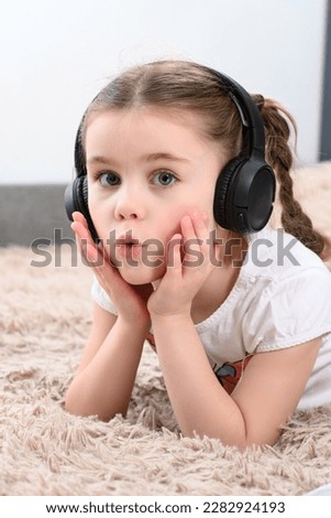 A little girl lies on the sofa and listens to music in headphones, a portrait of a child with headphones.