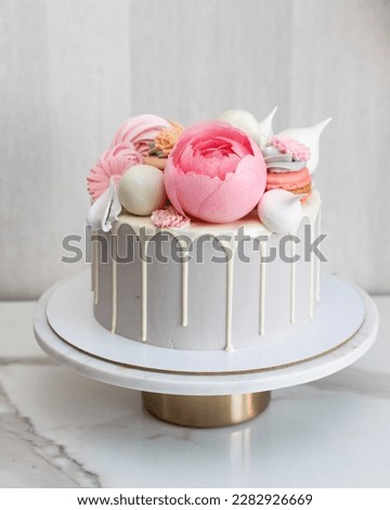 Beautiful and elegant grey cake decorated with melted white chocolate, macaroons, pink peony flower, cake pops and candies on marble cakestand