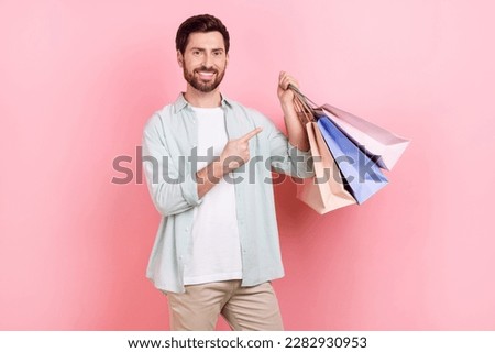 Photo portrait of attractive young man hold finger point shopping bags dressed stylish blue outfit isolated on pink color background