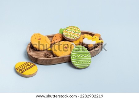 Easter gingerbread with icing on blue background. Gingerbread in the form of Easter eggs and chicken on wooden tray