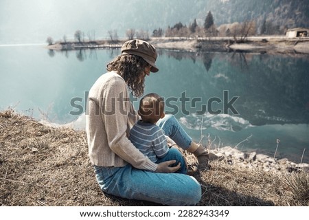 A young beautiful mother with a small child a boy walks near the lake and in the park. They smile and hug and admire nature.