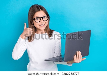 Photo of positive nice girl with long hairstyle wear white long sleeve showing thumb up hold laptop isolated on blue color background