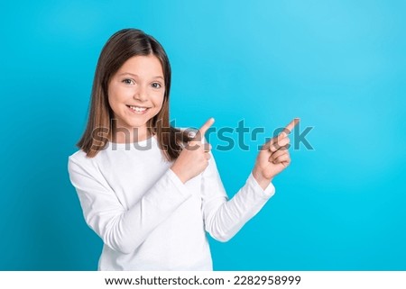 Photo portrait of cute little girl fingers point empty space dressed stylish white clothes isolated on blue color background